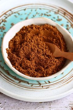 a white bowl filled with brown powder on top of a blue and white plate next to a wooden spoon