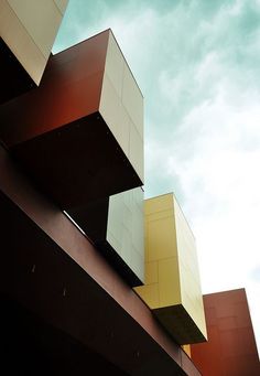 the side of a tall building with multiple windows on it's sides, against a cloudy blue sky