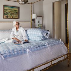 an elderly woman sitting on a bed with blue and white sheets, reading a book