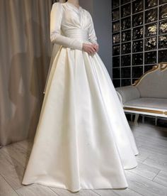 a woman in a white wedding dress standing next to a couch and window with curtains