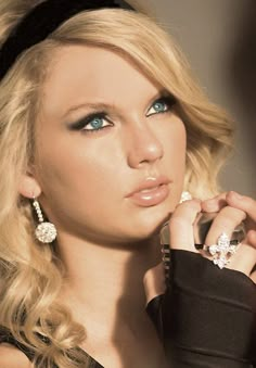 a beautiful blond woman with blue eyes and long hair wearing black gloves, holding her hand to her ear