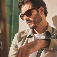 a man wearing sunglasses sitting down and looking at something on the table in front of him