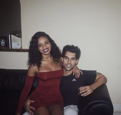 a man sitting next to a woman on top of a black couch in a living room