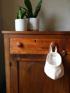 a white purse hanging from the side of a wooden cabinet next to a potted plant