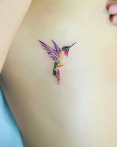 a small hummingbird tattoo on the side of a woman's stomach is shown