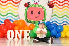 a baby sitting on the floor in front of balloons with a sign that says one