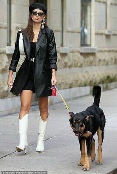 a woman is walking her dog down the street while wearing boots and knee high boots