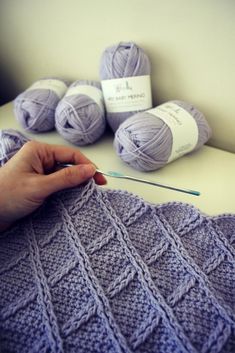 a person is knitting on a table with several balls of yarn