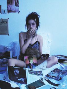 a woman sitting on top of a bed next to a pile of books and magazines