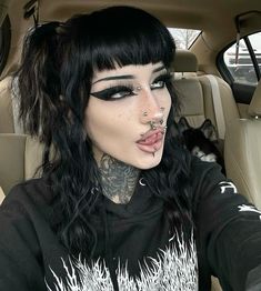 a woman with black hair and piercings on her nose sitting in the back seat of a car