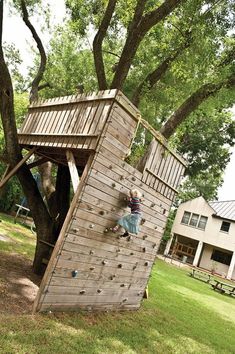 a child climbing up the side of a wooden structure in a yard with a tree