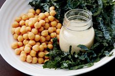 a white bowl filled with greens and chickpeas next to a jar of dressing