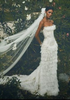 a woman in a white wedding dress with a veil over her head and flowers behind her