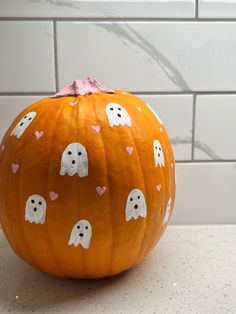 an orange pumpkin decorated with ghost faces and pink hearts on it's face, sitting on a counter