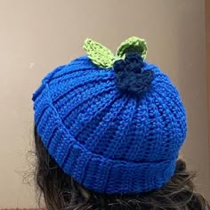 a woman wearing a blue knitted hat with a green leaf on it