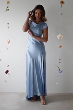 a woman in a long blue dress standing next to a wall with flowers on it