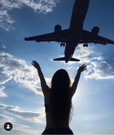 a woman standing in front of an airplane with her hands up to the sky above her head