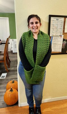 a woman standing in front of a wall wearing a green crocheted vest and boots