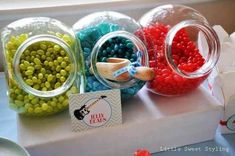 there are many different colored candies in glass jars on the table with tags around them