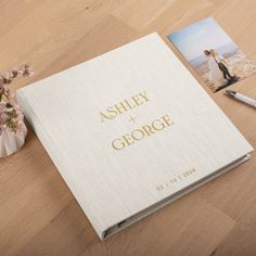 a wedding album and pen sitting on a wooden table next to a vase with flowers