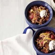 two blue bowls filled with chili and sour cream on top of a white tablecloth