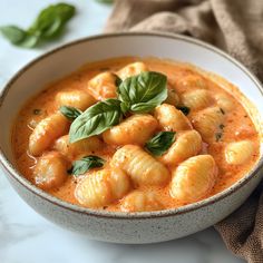 a white bowl filled with pasta and basil on top of a table next to a napkin