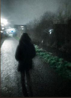 a person walking down a street at night in the rain with an umbrella over their head