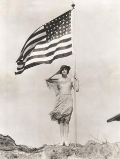 an old black and white photo of a woman holding the american flag on top of a hill