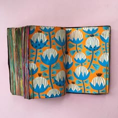 an open book with blue and white flowers on orange paper next to a pink wall