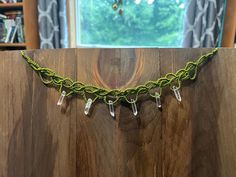 a green necklace is hanging on a wooden board in front of a bookcase and window