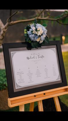 a black and white sign with flowers on it next to a wooden easel in front of a tree