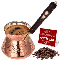 a copper coffee pot filled with liquid next to roasted coffee beans and a sign that reads handmade in anatolia