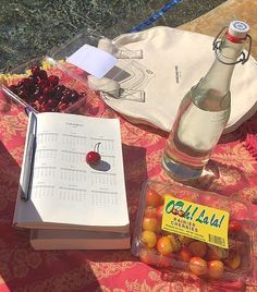 a bottle of water, notebook and cherries are sitting on a table next to the pool