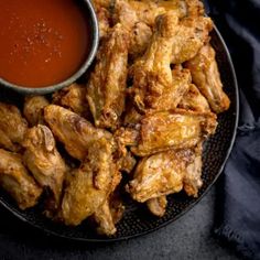 chicken wings with dipping sauce on a black plate next to a blue cloth and napkin