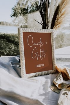 a card and gifts sign sitting on top of a bed next to dried flowers in a vase