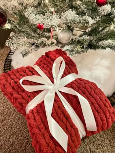 two red knitted heart shaped pillows with white ribbon tied around the edges, sitting in front of a christmas tree