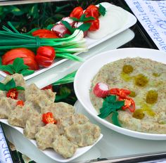 food items displayed on serving platters with vegetables and sauces in bowls next to each other