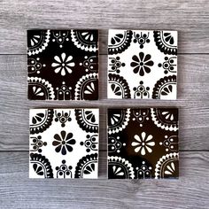 four black and white tile coasters sitting on top of a wooden table