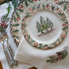 a christmas place setting with pine trees and holly on the plate, silverware and napkins