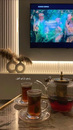 there is a tea pot and two cups on the table in front of a television