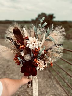 a person holding a bouquet with flowers and feathers on it's head in front of a fence