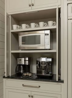 a coffee maker and some cups in a cabinet with white cupboards on the wall