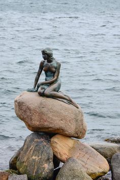 a statue sitting on top of a rock next to the ocean