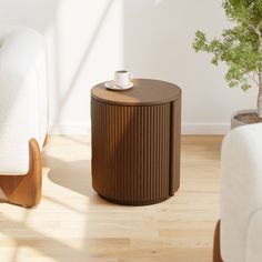 a coffee table with a cup on it next to a white couch and potted plant