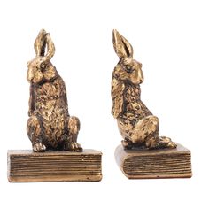 two golden rabbit figurines sitting next to each other on top of a book