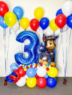 a birthday cake with balloons and an animal figure in the middle surrounded by blue, yellow, red, and white balloons