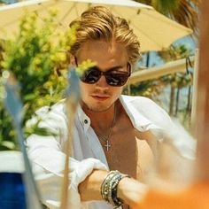 a young man wearing sunglasses sitting under an umbrella