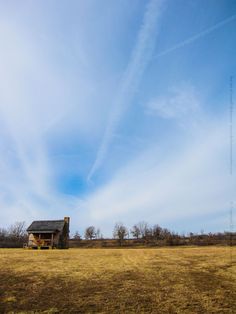 a large open field with a house in the middle and some clouds above it on a sunny day