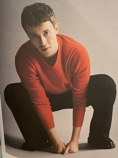 a young man in an orange sweater is posing for a photo with his hands on his knees