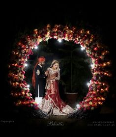 a bride and groom standing in front of a circular wreath with lights on the side